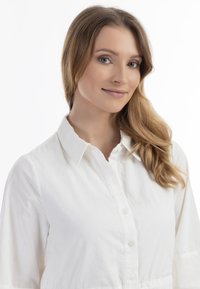 Hvid button-up skjorte med et tekstureret stof, krave og lange ærmer, der har en glat overflade og subtile syninger.