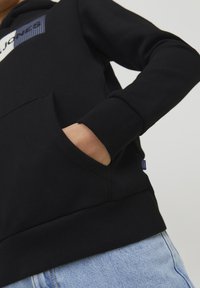 Felpa nera con cappuccio, dotata di tasca a marsupio, polsini a coste e design a fantasia blu e bianco sul petto. Tessuto morbido, vestibilità comoda.