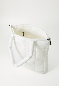 Sac cabas matelassé blanc avec fermeture éclair, doté de deux anses en tissu et d'un intérieur lisse avec une poche et une fermeture éclair en métal.