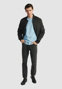 Czarna pikowana kurtka bomberka z zamykanymi na zamek kieszeniami, w połączeniu z jasnoniebieską koszulką z okrągłym dekoltem, ciemnymi dżinsami i czarnymi trampkami.