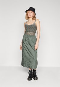 Lys grøn blonder topp med spagetti-stropper, kombinert med et langt, olivengrønt skjørt og svarte snøreboots, samt en svart bøttehatt.