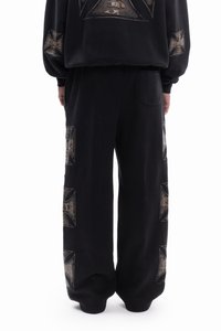 Black sweatshirt and pants set made of soft fabric, featuring large graphic prints in gold on sleeves and legs, relaxed fit, and a back pocket.