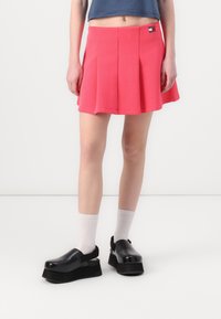 Jupe plissée rose avec une taille cintrée, assortie à des chaussures à plateforme noires. Les chaussures présentent une finition lisse et brillante ainsi qu'une bride de talon ajustable.