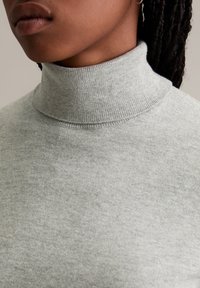 Grauer Rollkragenpullover aus weichem Stoff, mit einem gerippten Kragen und glatter Textur, aus einer Nahaufnahme, die das Design hervorhebt.