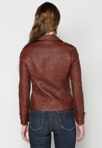 Giubbotto in ecopelle marrone con un design aderente, dotato di colletto classico, cuciture strutturate e spalline con bottoni. Vista posteriore.