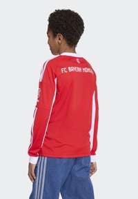 Rode FC Bayern München shirt met witte accenten en lange mouwen, met de teamnaam op de achterkant. Draag het met blauwe denim broek.
