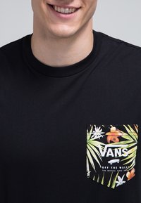 Černé bavlněné tričko s barevnou kapsou s tropickým vzorem listů a logem Vans. Klasický design s kulatým výstřihem.