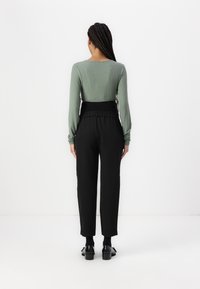 Haut à manches longues vert rayé avec un col rond, associé à un pantalon noir taille haute et des chaussures à talons noires, vu de dos.