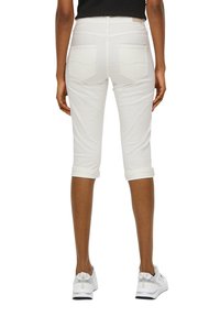 Valkoiset lyhyet farkut käännetyillä lahkeilla, joissa on kaksi takataskua ja sileä pinta. Yhdistetty valkoisten urheilujalkineiden kanssa.