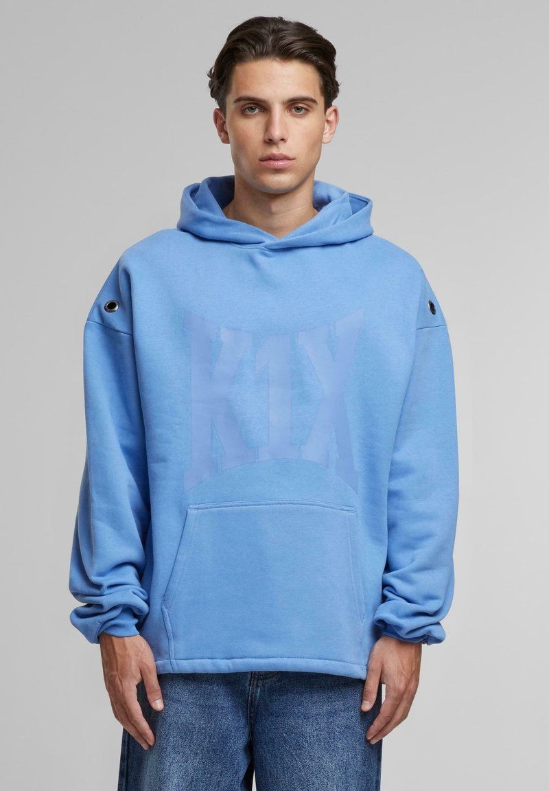 Sudadera azul claro de tejido suave, con bolsillo tipo canguro, corte relajado y detalle de ojales en el hombro izquierdo. Gran impresión de logo.