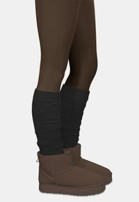 Braune Wildleder-Stiefeletten mit weichem Innenfutter, kombiniert mit dunklen gestrickten Beinwärmern, getragen über braunen Leggings.