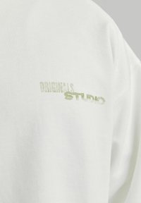 Un hanorac alb din bumbac, prezentând textul "ORIGINALS" și "STUDIO" imprimate în verde deschis, cu un design clasic de gât rotund.