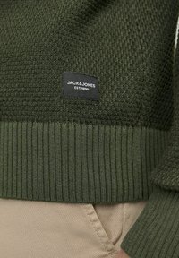 Olivovo zelený pletený sveter s textúrovanou hornou časťou a rebrovaným lemom. Obsahuje čiernu nášivku "JACK & JONES".