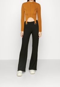 Brun, rippad långärmad topp med utskärning och ringdetaljer, matchad med texturerade svarta vida byxor och vita sneakers.