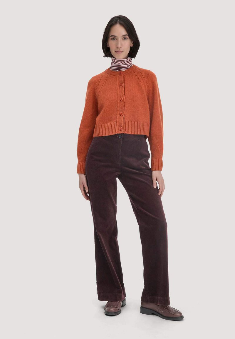 Oranje gebreide cardigan met ronde hals en knopen, gecombineerd met donkere bordeaux kleurige wijde corduroy broek en bruine instappers.