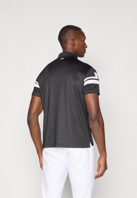 Μαύρο κοντομάνικο πουκάμισο πόλο με γιακά και λευκές λεπτομέρειες στις ώμους. Διαθέτει λογότυπο στο πίσω μέρος του λαιμού και λεπτομέρεια αεραγωγού στο πλάι.