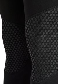 Czarne legginsy sportowe mają teksturowany panel z siateczki z sześcio kątnymi wzorami na kolanach, uzupełniony gładkim, elastycznym materiałem.