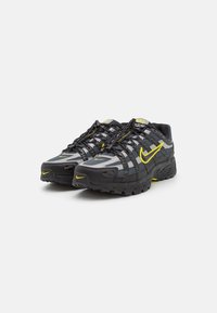 Paire de chaussures de course Nike noires et grises avec des accents jaunes et des lacets, légèrement inclinées vers la droite sur fond blanc.