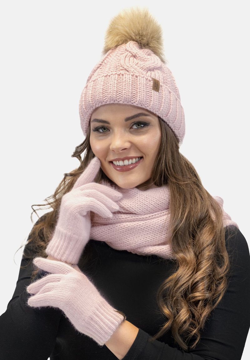 Beanie rosa lavorato a maglia con pompon in pelliccia, guanti coordinati e una sciarpa testurizzata. Presenta un motivo a treccia e polsini a coste.