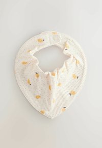 Babero redondo blanco para bebé con pequeños puntos negros y patrones de limones amarillos, asegurado con un solo botón a presión blanco.