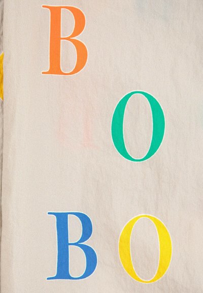 Katoenen stof met gedurfde bedrukte letters: oranje "B," teal "O," blauwe "B," en gele "O" op een lichtbeige achtergrond.