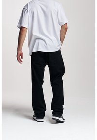 Svarta denimjeans och en vit t-shirt med kort ärm. Jeanssen har en lös passform, medan t-shirten är enfärgad med rund halsringning.