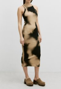 Bodycon-Kleid in beigem und schwarzem Batikmuster, ärmellos mit rundem Ausschnitt. Kombiniert mit braunen Clogs mit dicken Absätzen.