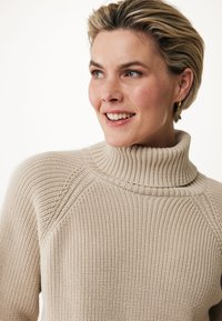 Beige turtleneck sweater with ribbed texture, featuring a high collar and raglan sleeves, displayed against a light background.