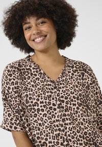 Blusa a stampa leopardata realizzata in tessuto leggero, presenta un collo arricciato e maniche corte, con bottoni neri lungo il davanti.