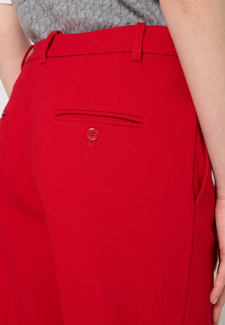 Pantaloni rossi su misura con fronte piatto, passanti per cintura e una tasca sul retro con bottone. Texture liscia con una vestibilità strutturata.