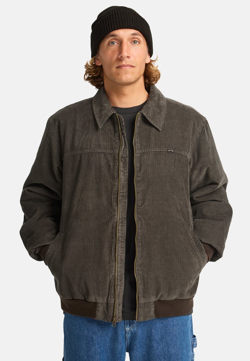 Giacca in corduroy di colore grigio scuro, con zip frontale, polsini e colletto a coste, tasche laterali e un sottile logo del marchio sul petto.