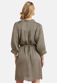 Kurzes Kleid mit einem schwarz-creamfarbenen Zickzackmuster, tailliert mit Puffärmeln für mehr Volumen. Rückansicht gezeigt.
