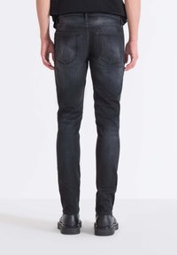 Schwarze Denim-Jeans im Slim-Fit, mit hinteren Taschen, dezentem Ausbleichen und einem sauberen Ästhetik. Der Stoff hat eine glatte Textur.