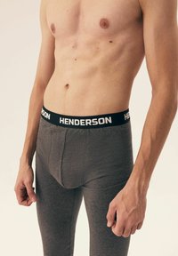 Gray leggings with a soft texture, featuring a black waistband labeled "HENDERSON." The design is fitted, covering the waist to ankles.