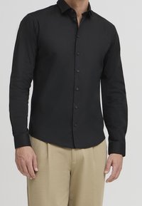 Zwarte lange mouwen shirt gemaakt van gladde stof, met een slim fit, knop-down kraag en zwarte knopen. Draagt met beige broek.