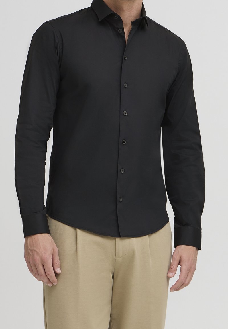 Zwarte lange mouwen shirt gemaakt van gladde stof, met een slim fit, knop-down kraag en zwarte knopen. Draagt met beige broek.