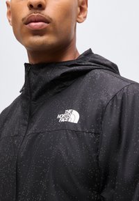 Νεαρός που φοράει μαύρο αδιάβροχο μπουφάν North Face με κουκούλα, κοντινό πλάνο που δείχνει σταγόνες νερού στον ύφασμα του μπουφάν.