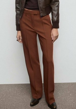 Pantalones marrones ajustados con un diseño de pierna recta, textura suave y costuras planchadas sutiles. Combinados con una chaqueta oscura y zapatos negros.