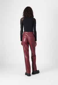 Pantalons en simili cuir bourgogne taille haute, avec poches arrière et texture lisse. Portés avec un haut noir ajusté à manches longues.