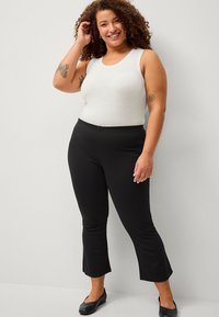 Top bianco senza maniche con scollatura rotonda abbinato a pantaloni neri elasticizzati a campana. L'outfit presenta una texture liscia e un design aderente.