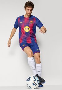 FC Barcelona-tröja och shorts, blå med mörkröda ränder, med en gul Spotify-logotyp. Svarta fotbollsskor, vita strumpor och en mönstrad boll.