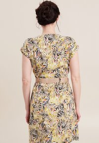 Bloemenjurk in geel, zwart en rood. Korte mouwen, aansluitende taille met een geweven beige riem. Zachte stof met een bladmotief.
