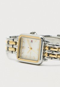 Štvorcové strieborné a zlaté náramkové hodinky s bielym ciferníkom, zlatými rímskymi číslicami a rukami, a dvojfarebným prepojeným kovovým remienkom, ukazujúce 10:10:38.