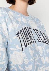 Světle modrý sweatshirt s květinovým vzorem a výšivkou "TOMMY JEANS" v námořnické barvě. Vyrobeno z měkkého, strukturovaného materiálu s kulatým výstřihem.