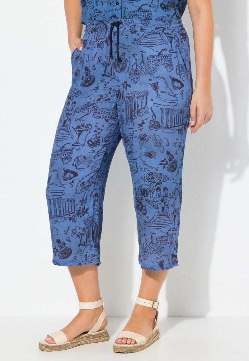 Blauwe cropped broeken met een tunneltaille, versierd met een grafisch patroon van bezienswaardigheden en eten. Zachte stof met een relaxte pasvorm. Draag met beige sandalen.