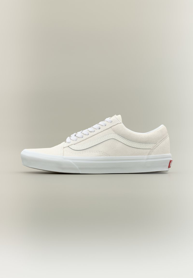 Witte suède sneaker met lage schacht, witte veters, zijstreep, dikke witte rubberen zool en rood haktlogo tegen een effen achtergrond.