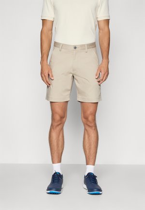 Beige shorts i en avslappnad passform med knappstängning, bältesöglor och sidofickor. Matchat med blå sportskor och vita strumpor.