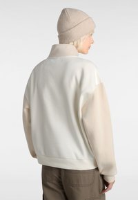 Sweatshirt color block crème et beige avec un col haut, des poignets et un ourlet côtelés. Tissu doux, coupe ample, design minimaliste et sans marquage visible.