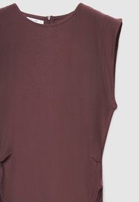 Robe sans manches bordeaux avec une finition texturée, encolure ronde et fermeture éclair discrète au dos. Met en valeur une silhouette fluide.