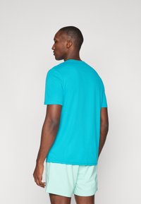 Türkises T-Shirt mit kurzen Ärmeln und Rundhalsausschnitt, glatter Textur und genähtem Saum, getragen mit leichten Mint-Shorts.